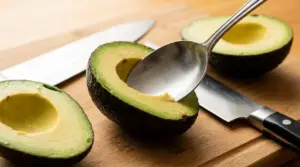 Metà di avocado su tagliere con cucchiaio e coltelli, pronta per essere tagliata e mangiata