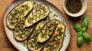 Melanzane grigliate condite con mix di erbe, olio e aglio su un piatto, con ciotolina di salsa a lato